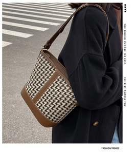 Detail of houndstooth bucket bag featuring brown leather trim and slim shoulder strap