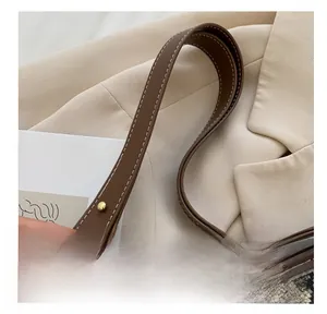 Close-up of brown leather handle with white stitching and gold rivet on houndstooth bag