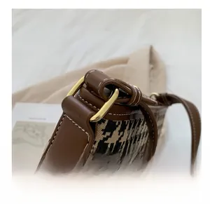 Detail of golden D-ring hardware and white stitching on houndstooth bucket bag