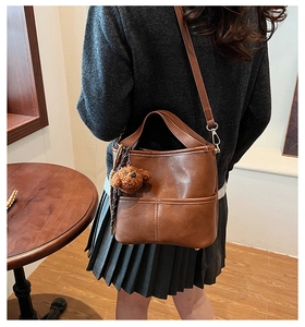 Detail of dark brown leather bucket bag with a plush bear charm on adjustable strap