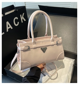 Detail of light pink patent leather handbag with a metallic triangle plate and dual handles