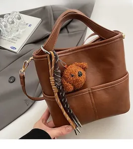 Detail of dark brown bucket bag with plush bear charm on elegant grey fabric