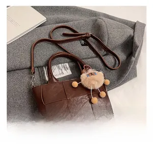 Détail du sac seau marron en cuir tressé avec pendentif en peluche sur manteau gris