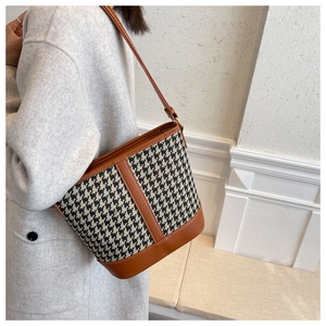 Detail of houndstooth bucket bag with brown leather trim and metal hardware accents