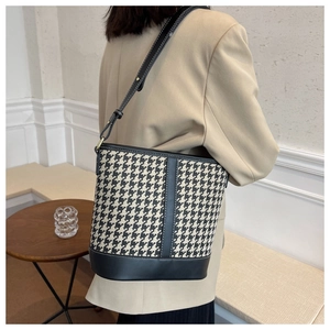 Detail of houndstooth bucket bag with black leather trim worn on the shoulder
