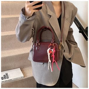 Detail of burgundy Boston bag with metallic hardware and decorative woven ornament