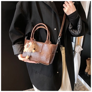 Détail du sac seau en cuir tressé marron foncé avec poignée et joli pendentif peluche