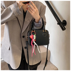 Model wearing a black leather Boston bag with white stitching and a woven charm