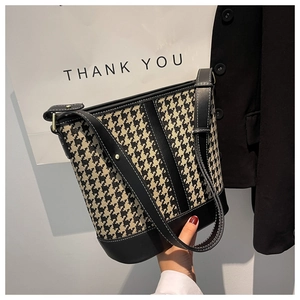 Detail of houndstooth bucket bag with black leather trim and adjustable strap in hand