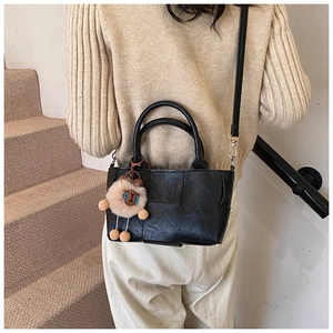 Détail du sac seau noir tressé avec breloque en peluche porté par un mannequin chic
