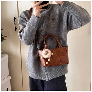 Sac seau marron en cuir tressé avec charm lion en peluche porté par un mannequin