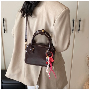 Detail of dark brown glossy leather square bag with decorative charm on beige blazer