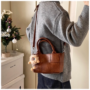 Détail d'un sac seau tressé marron avec charm lion en peluche et bandoulière réglable