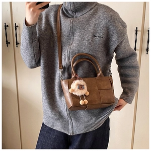 Détail d'un sac seau tressé marron avec charme en peluche et bandoulière amovible