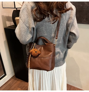 Detailed view of coffee brown leather bucket bag with cute plush bear pendant accessory