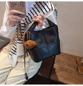 Detail of black PU leather bucket bag with stitch accents and cute bear pendant charm