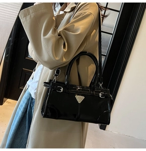 Detail of black patent leather crossbody bag with triangular logo and silver hardware