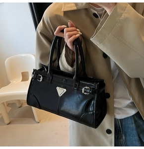 Detail of silver triangle plaque and side buckle straps on a black polished leather tote