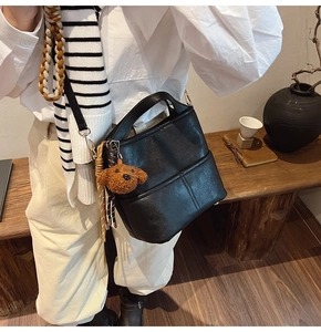 Detail of black leather bucket bag with decorative stitching and brown teddy charm