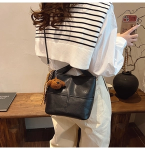Detail shot of a black bucket bag with a brown bear charm shown in a lifestyle setting