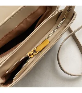 Close-up of beige shoulder bag with smooth golden metal zipper and brown fabric interior