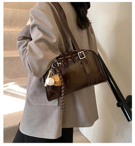 Detail of dark brown glossy underarm bag with unique baseball charm on model