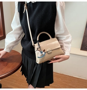 Detail of beige glossy leather handbag featuring a metal clasp and horse charm