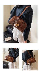 Close-up of brown glossy leather tote with vintage metal buckle and baseball charm