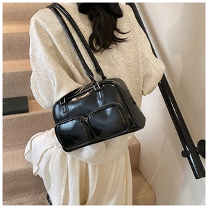 Close-up of black glossy shoulder bag with dual front zipper pockets and slim straps