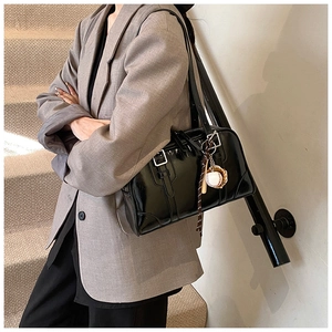 Detail of black glossy Boston bag with silver buckles and creative baseball pendant charm