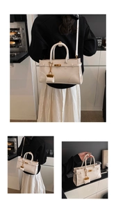 Detail of white leather handbag with metal lock, small pendant, and detachable shoulder strap