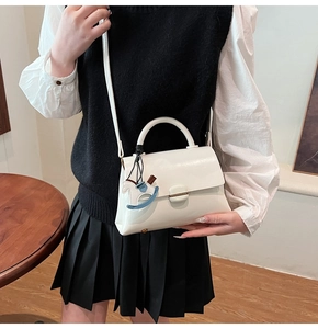 White patent leather handbag with a blue rocking horse charm shown on a fashion model