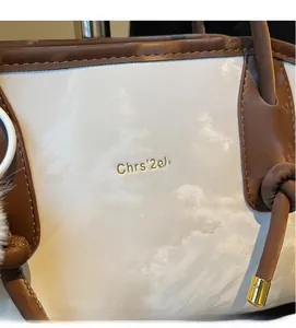 Detail of white glossy leather tote with brown trim and golden brand logo lettering