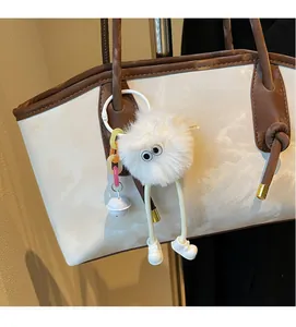Close-up of white plush monster keychain with long legs and bell on a tote bag