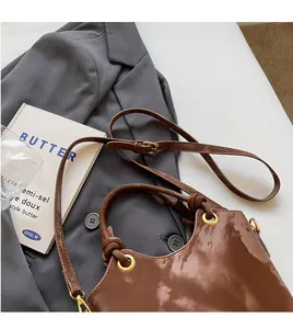 Detail einer glänzenden braunen Handtasche mit goldenen Ringen und verstellbarem Tragegurt