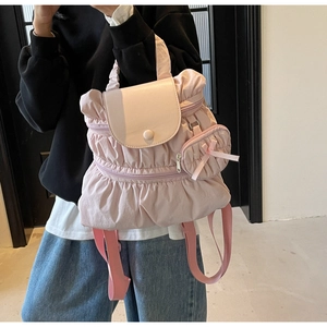 Pink pleated nylon backpack with cute bow charm and rounded flap detail worn by model