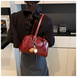 Detail of burgundy leather bowling bag with creative baseball charm and adjustable strap