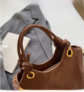 Detail einer braunen glänzenden Handtasche mit geknotetem Griff und goldenen Ösen