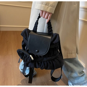 Detail of black pleated nylon backpack featuring a leather flap and small round coin pouch