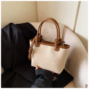 Détail du sac cabas tissé montrant la texture beige et l'anse en cuir marron