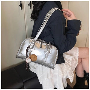 Metallic silver Boston bag with baseball charm shown worn by model in a street style setting