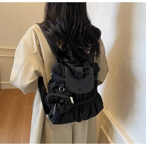 Detailed back view of a black pleated nylon backpack on a model wearing a trench coat