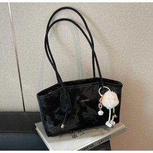 Detail of black glossy tote bag with metal logo and soft white plush charm on book