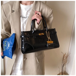 Detail of glossy black leather handbag with gold metal lock and vintage hardware