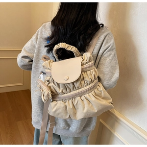 Detail of beige pleated backpack featuring a magnetic flap and a mini coin purse charm