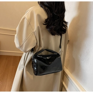 Detail of vintage black oiled leather pillow bag with embossed letters on a beige coat
