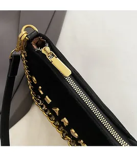 Close-up of smooth gold metal zipper and durable chain on black crossbody bag