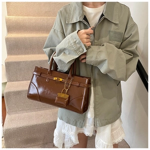 Close-up of brown patent leather handbag featuring gold buckle and mini padlock detail