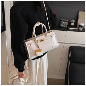Detail of white leather handbag featuring metal twist lock and a mini charm accessory