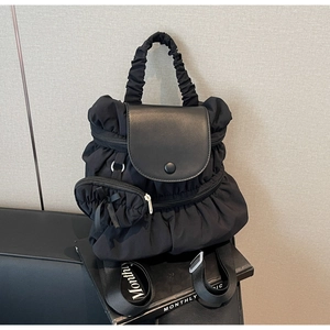 Detail of black pleated nylon backpack featuring a leather flap and decorative bow pouch